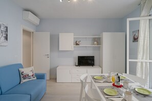 A modern room with a blue sofa, a dining table set with plates and glasses, a white cabinet, and a flat-screen TV.