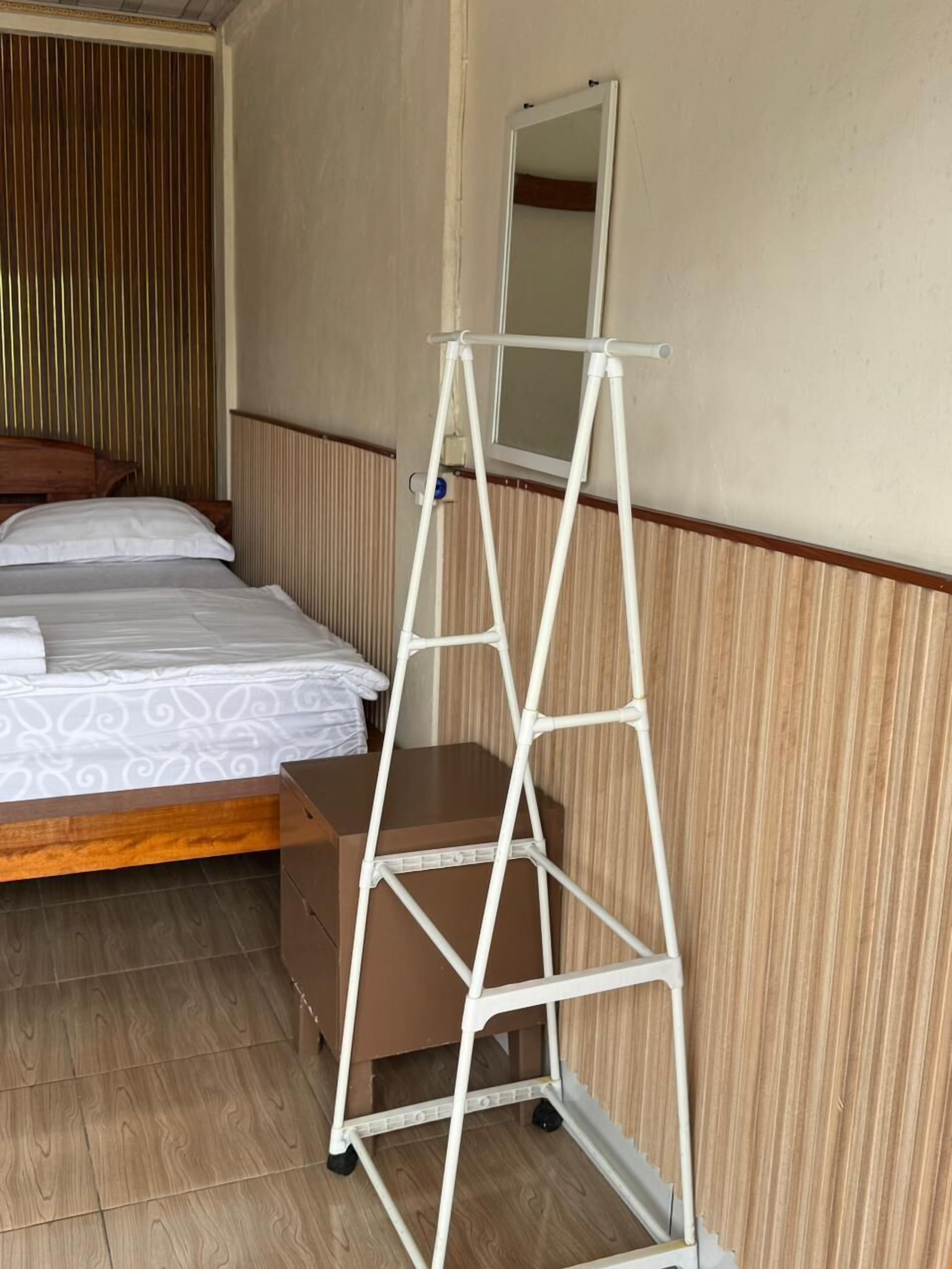 A room with a bed, a wooden dresser, a white metal shelf unit, and a mirror.