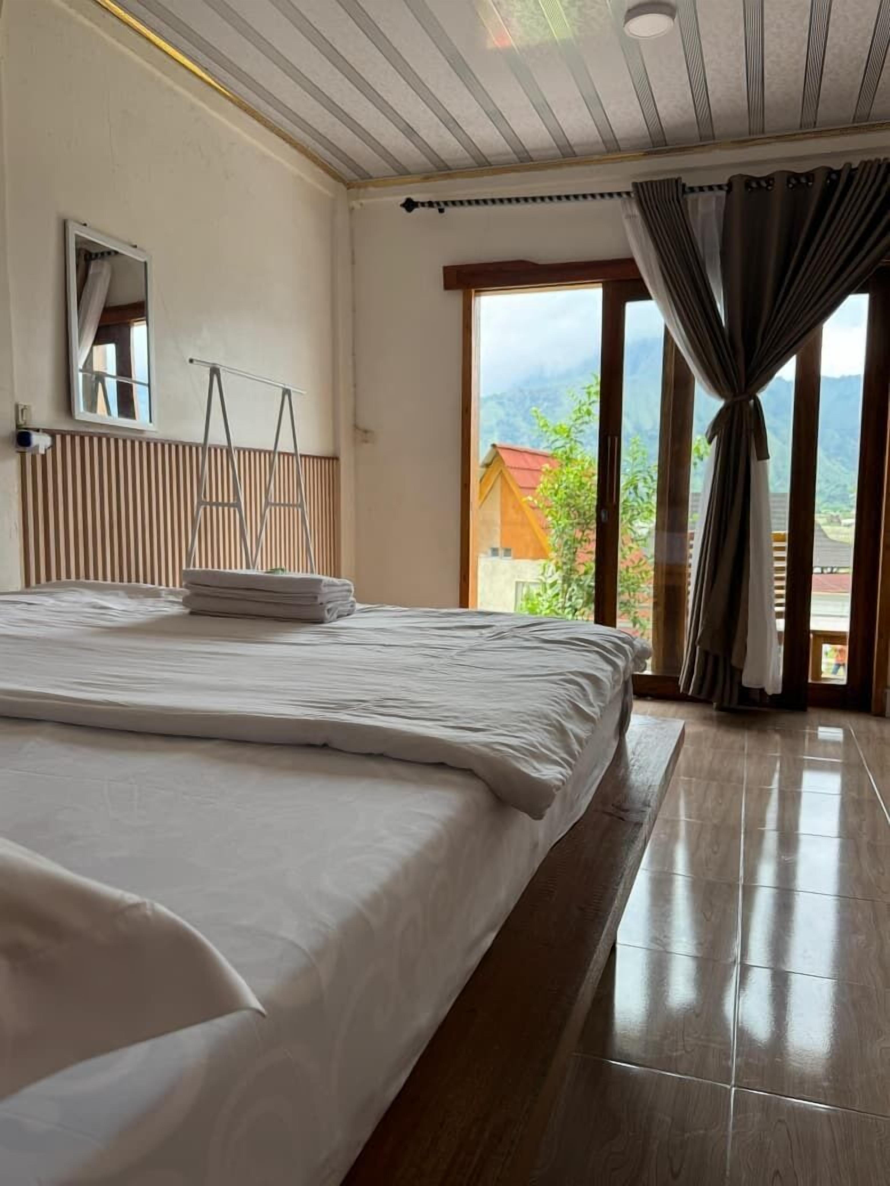 Une chambre avec un grand lit, une fenêtre avec des rideaux, un plancher en bois et une vue sur les montagnes.