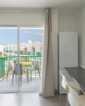 Ein Balkon mit Tisch und Stühlen, einem Kühlschrank und Blick auf Gebäude sowie eine Flagge.