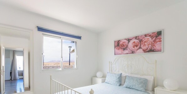 Una camera da letto con un letto, un comodino, un quadro appeso al muro e una finestra con vista sul paesaggio desertico.