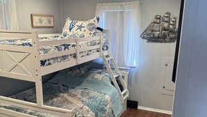 Una cama litera con temática náutica, una ventana con cortinas y una decoración de barco en la pared.