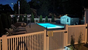 Una piscina con muelle de madera y sillones de descanso, rodeada de una cerca y árboles.