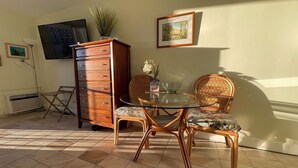 Uma área de refeições com mesa de vidro, cadeiras de vime, um armário de madeira e um quadro pendurado na parede.