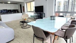 Ein modernes Wohnzimmer mit Glastisch, grauem Sofa und Fernseher auf einem Schrank.