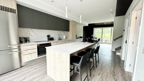 A modern kitchen with a central island, dark cabinets, and a large window providing natural light.