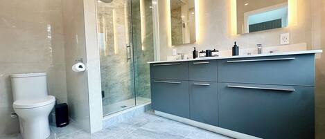 A modern bathroom with a glass-enclosed shower, a toilet, and a vanity with drawers and a mirror.