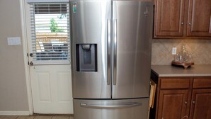 A stainless steel refrigerator with a water dispenser, a white door, and wooden cabinets in the background. - Cozy 4BR Retreat Near Randolph AFB & Ft Sam (Converse)