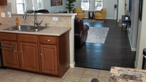 A modern kitchen with a built-in sink and wooden cabinets, a living room with a sofa and chairs, and a dining area with a table and chairs. - Cozy 4BR Retreat Near Randolph AFB & Ft Sam (Converse)