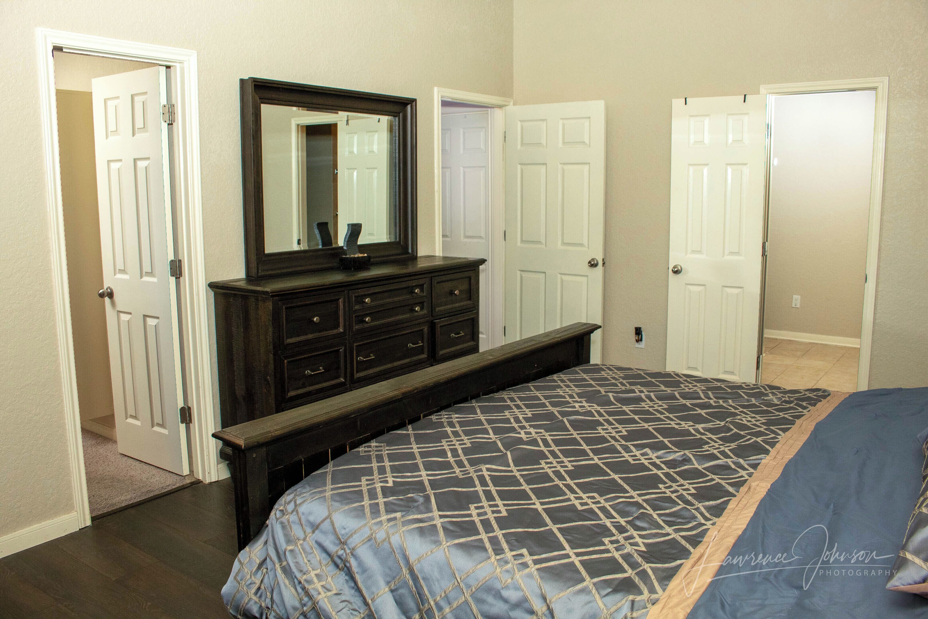 A bedroom with a bed, dresser, and two doors.