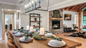 A dining area with a long wooden table set for a meal, a fireplace, and a stone wall. - 6BR-Epic Yard-Game And Movie Rooms (Sevierville)
