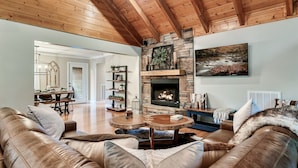 A cozy living room with a leather sofa, a round wooden coffee table, and a stone fireplace. - 6BR-Epic Yard-Game And Movie Rooms (Sevierville)