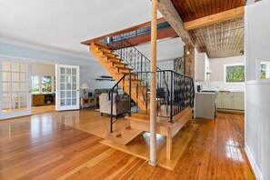 A spacious living area with a wooden staircase, a cat tree, and a kitchen area. - Golden Field Farmhouse @stayinpec (Prince Edward)
