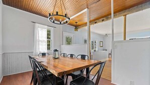 Un coin repas avec une table et des chaises en bois, un lustre et une vue sur la cuisine.
