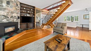 Un salon spacieux avec une cheminée en pierre, un escalier en bois et un coin salon confortable.
