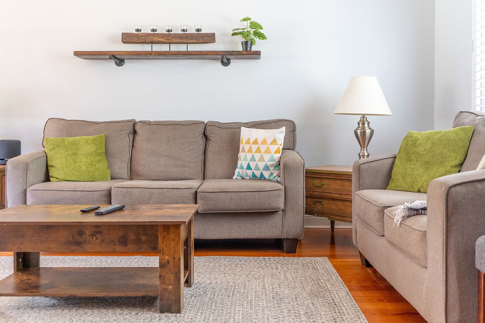Un salon avec un canapé, une table basse et une table d’appoint. Il y a une lampe sur la table d’appoint et une plante accrochée au mur.