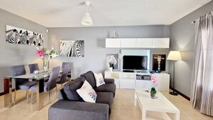Ein modernes Wohnzimmer mit einem grauen Sofa, einem weißen Couchtisch und einem Essbereich mit einem Glastisch und Stühlen.