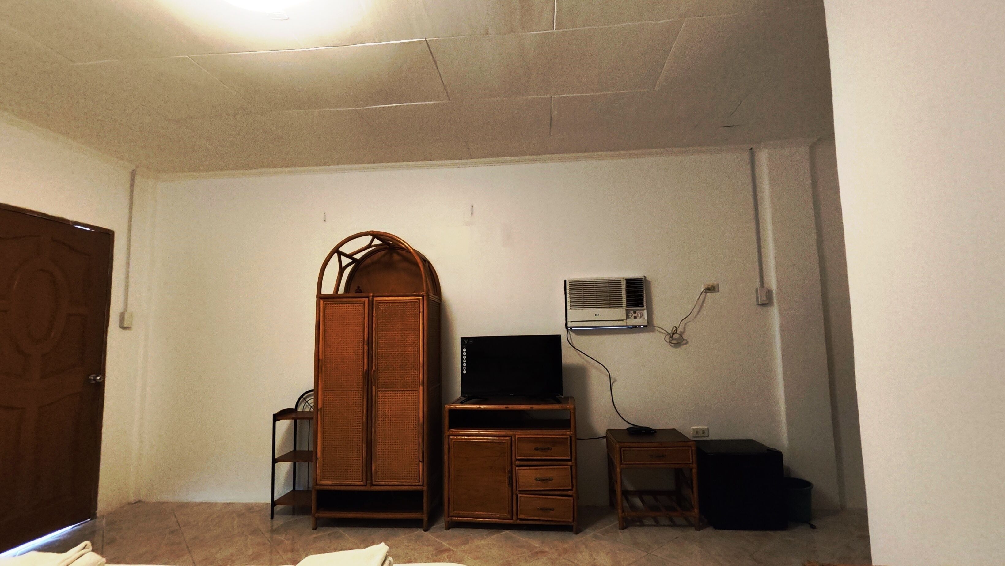 A room with a wardrobe, a desk with a computer, a small table, and an air conditioning unit.