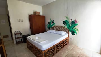 Una habitación con una cama, un armario de madera y una pared decorada con un mural tropical.