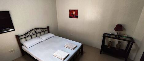 A bedroom with a bed, a bedside table with a lamp, and a small painting on the wall.