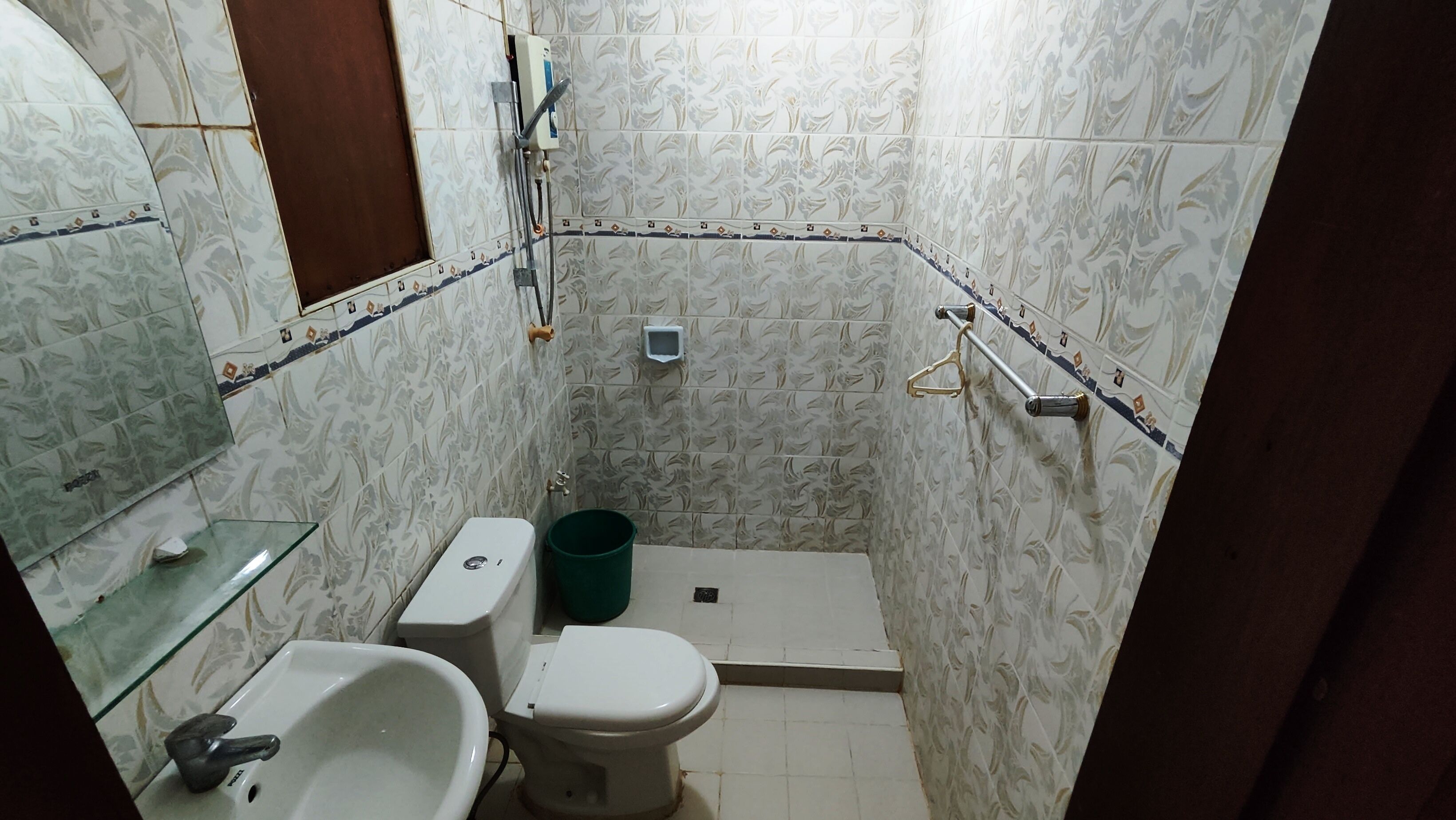 Un baño pequeño con inodoro, bidé y lavamanos. Cuenta con zona de ducha con puerta de vidrio y un perchero para toallas.