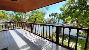 A balcony with a tiled floor and a wooden railing, overlooking a garden and a body of water.