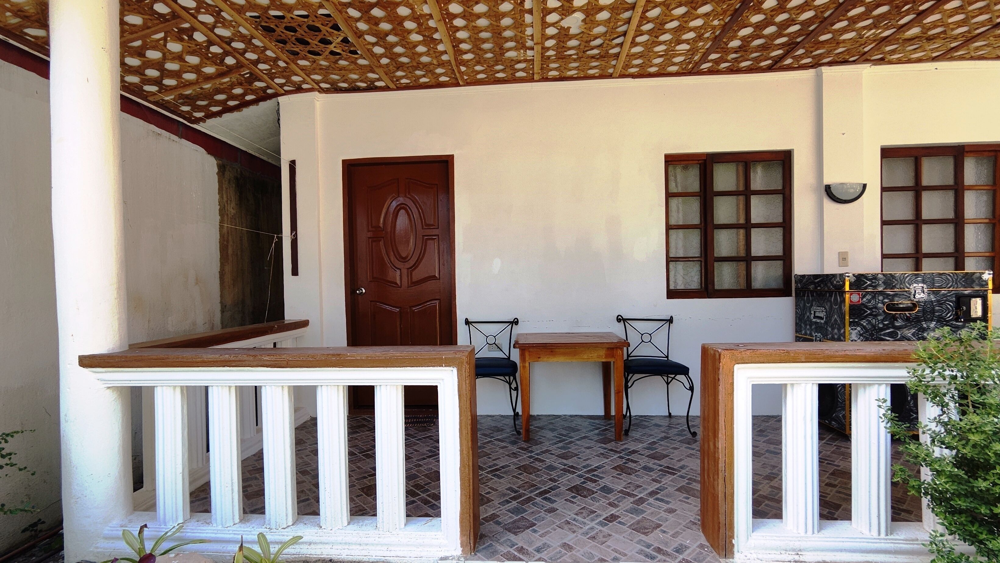 Quarto com porta de madeira, duas janelas com vidro fosco, soalho ladrilhado e uma pequena mesa com cadeiras.