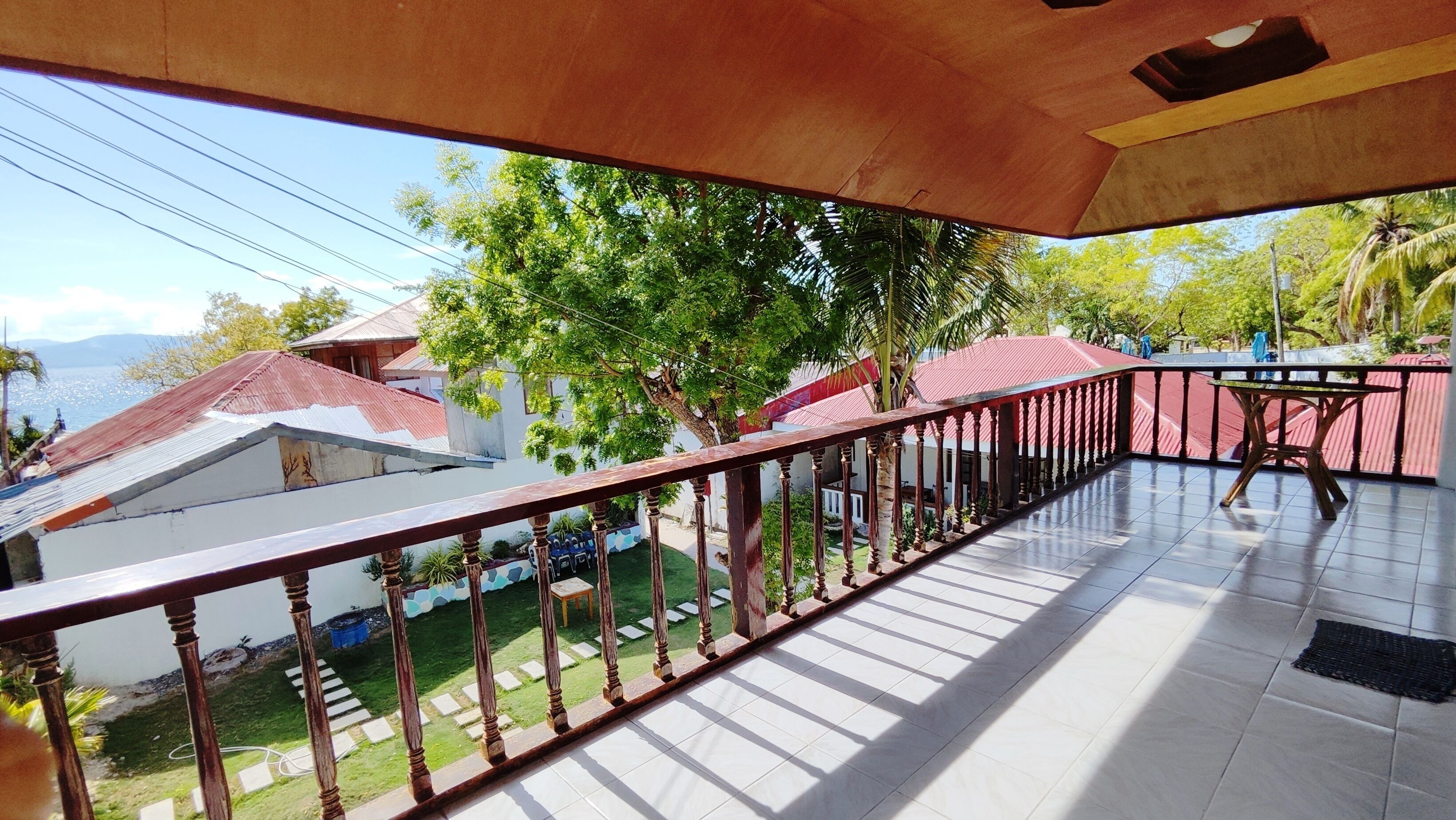 A balcony with a tiled floor and a wooden railing. There are houses with red roofs in the background.