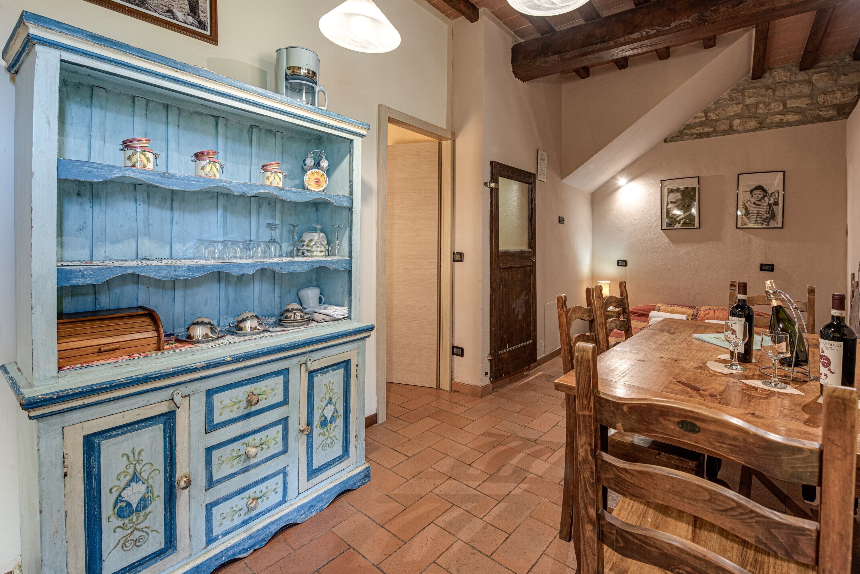 Un coin repas avec une table en bois dressée pour deux personnes, un buffet bleu orné d’objets décoratifs et un mur en pierre.