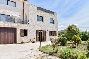 Ein zweistöckiges Gebäude mit Balkon, Garage und Garten mit verschiedenen Pflanzen und Blumen.