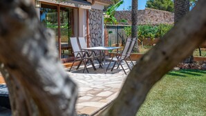 Um pátio externo com mesa e cadeiras, uma parede de pedra e vista para um jardim.