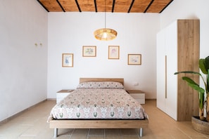 Une chambre à coucher comprenant un lit, des tables de chevet, un luminaire suspendu, des œuvres d’art encadrées et une plante en pot.