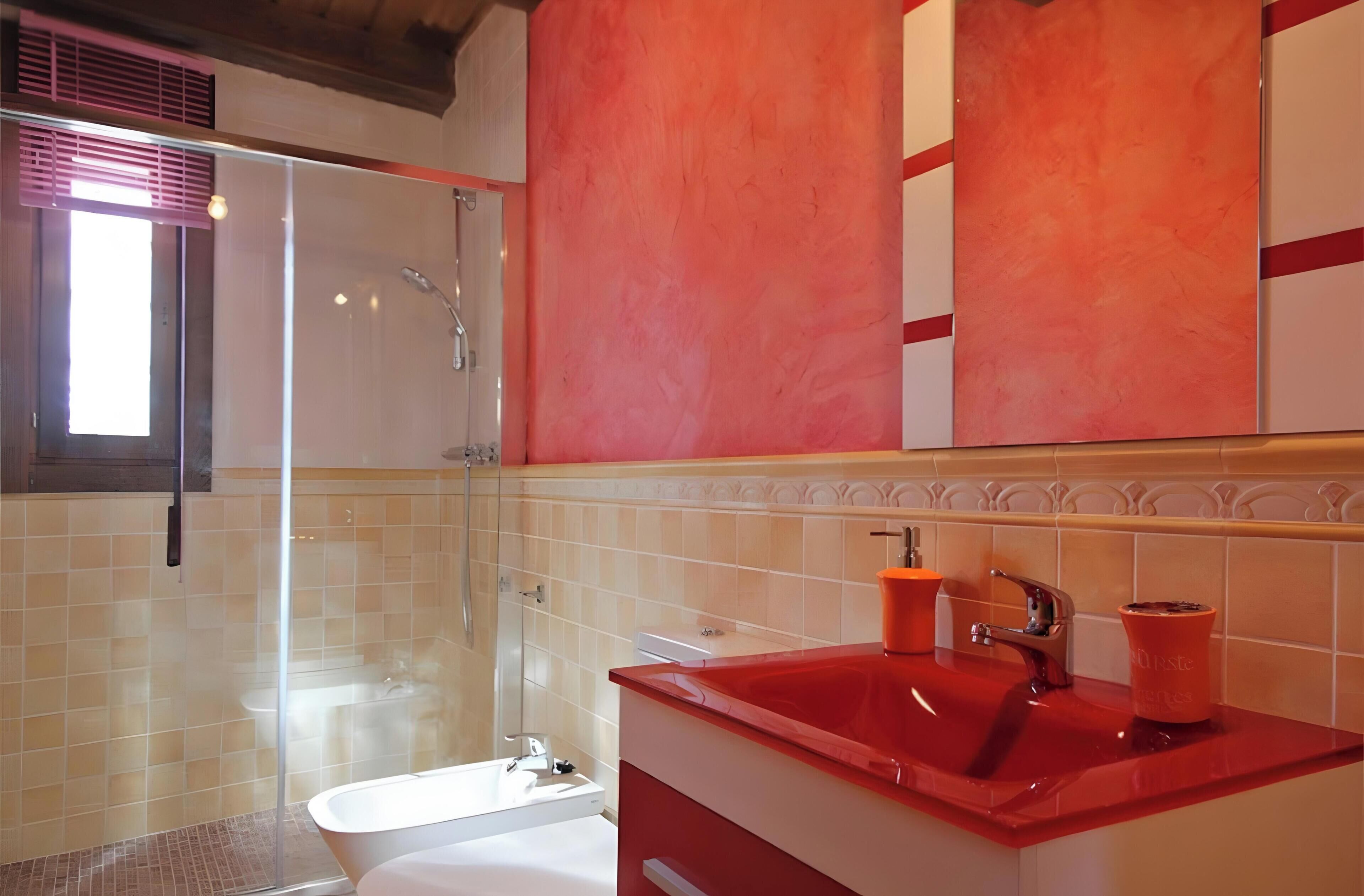 Un bagno moderno con box doccia in vetro, una vasca da bagno bianca e un lavandino rosso.