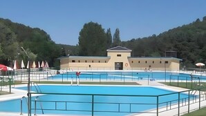 Zona de piscina con un edificio al fondo, rodeada de árboles.