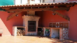 Un patio con piso de baldosas, chimenea de ladrillo y un área techada con estructura de vigas de madera.