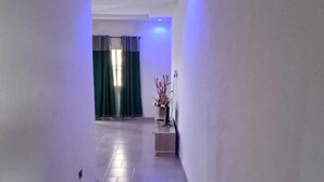A hallway with a tiled floor, a potted plant, and a window with curtains. - Apartment - Sleeps 4 - Parking - Wi-Fi (Ibeju Lekki)