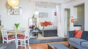A modern living room with a grey sofa, a dining table with chairs, a small kitchen area, and a bedroom with a bed and a nightstand. - 1 Bed Studio Sleeps 4 - Seaside, Dog Friendly (Bridlington)