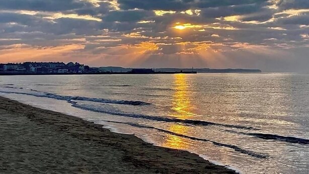 A beach with a calm sea reflecting the sky, a distant shoreline with buildings, and a cloudy sky with the sun setting or rising. - 1 Bed Studio Sleeps 4 - Seaside, Dog Friendly (Bridlington)