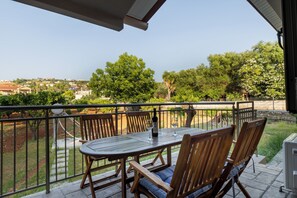 A patio with a table and chairs, overlooking a garden and a distant town.