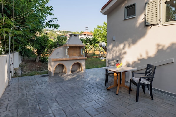 An outdoor patio with a barbecue grill, a table, and two chairs.