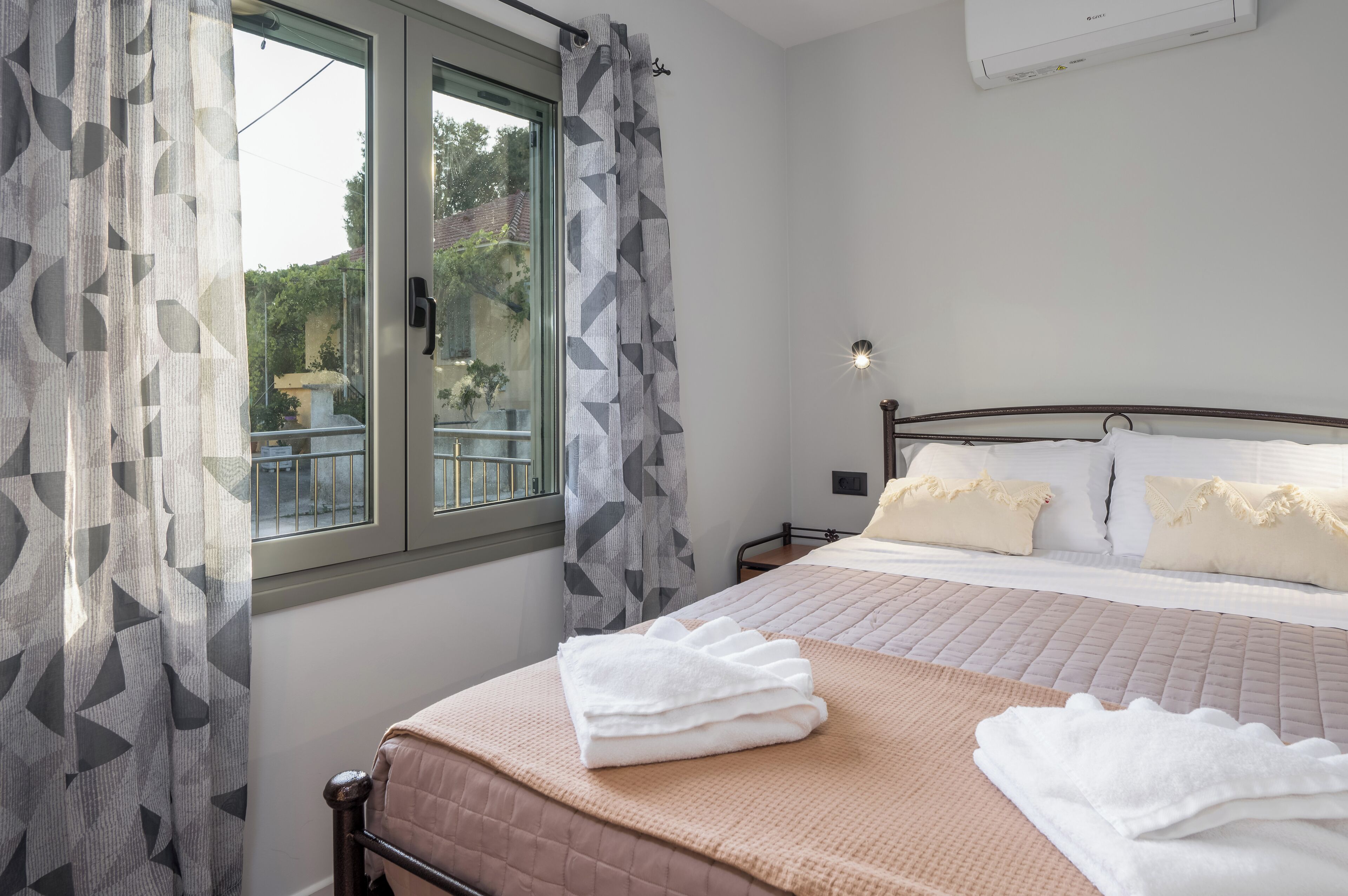 Una habitación de hotel con cama, ventana con cortinas, mesita de noche y equipo de aire acondicionado.