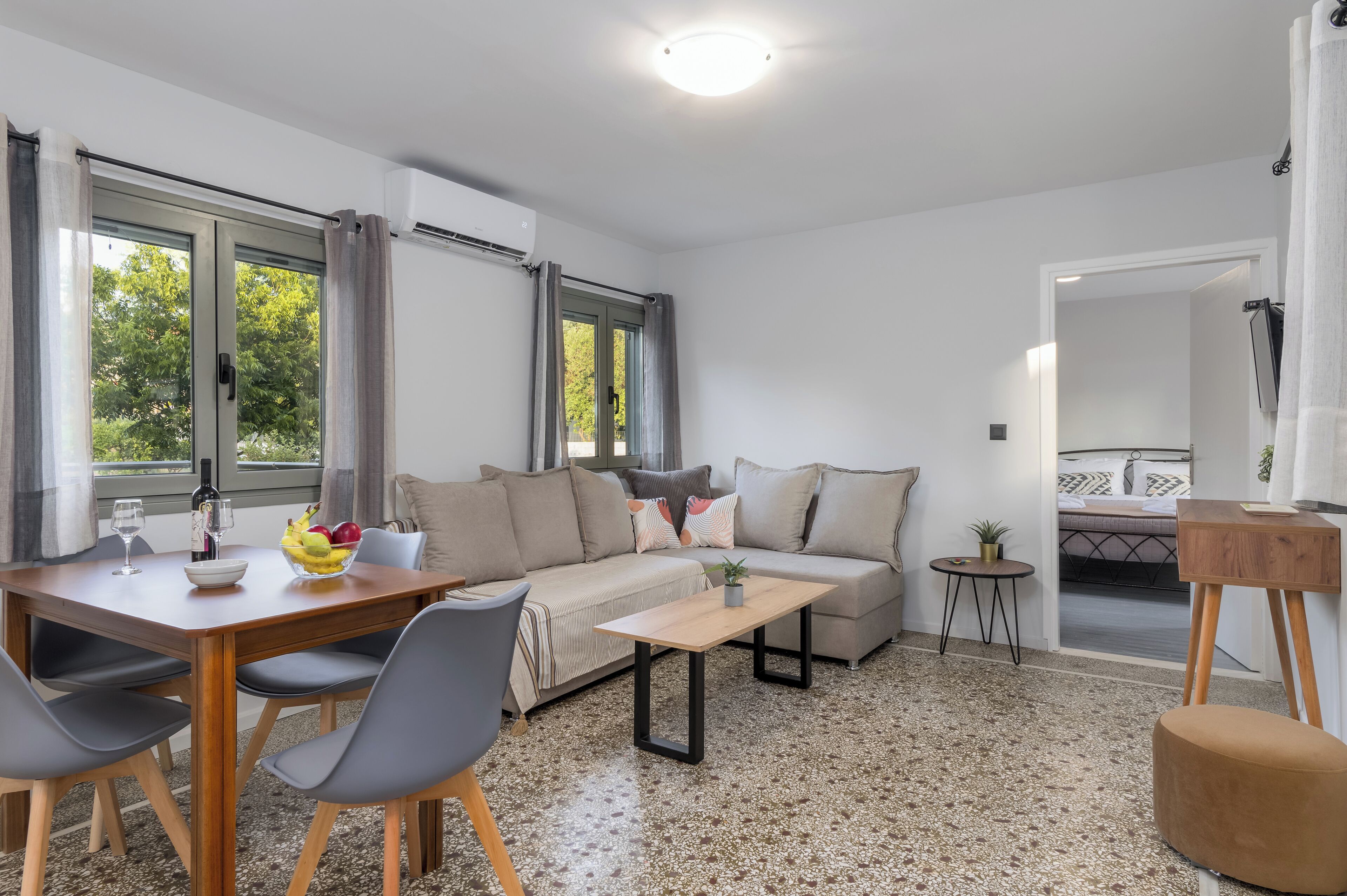 Una sala moderna con sofá, mesa de centro y mesa de comedor. Hay ventanas con cortinas, una mesita auxiliar y una planta.