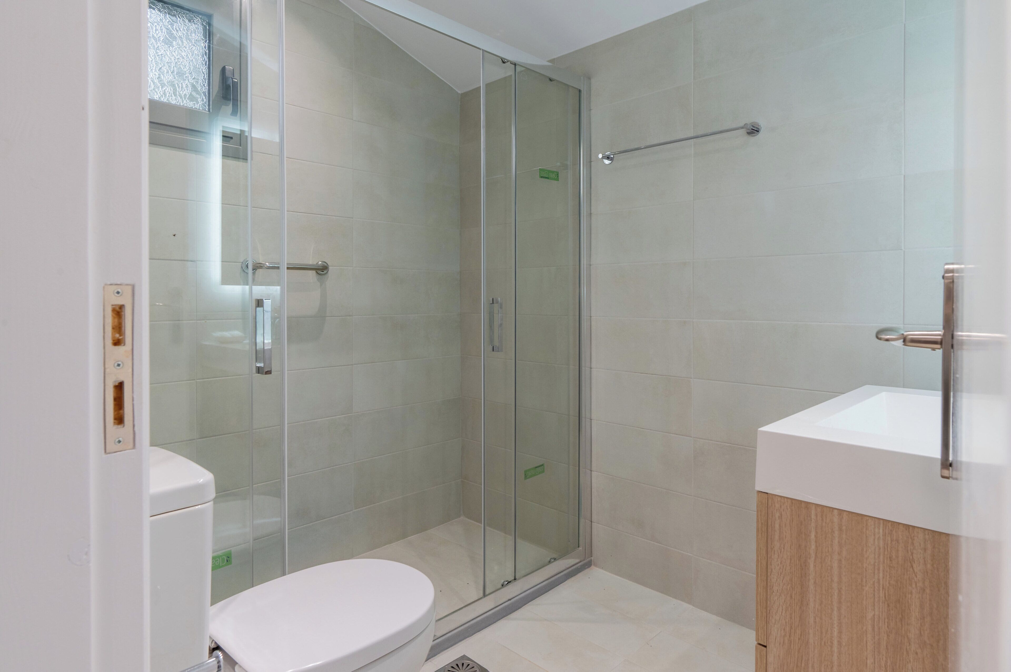 Un baño moderno con ducha acristalada, inodoro blanco y tocador de madera con lavamanos.