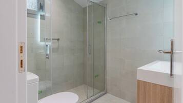Un baño moderno con ducha acristalada, inodoro blanco y tocador de madera con lavamanos.