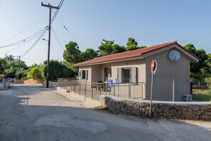 A small, single-story building with a red-tiled roof, a stone wall, and a metal fence.