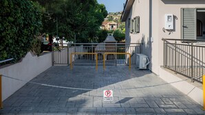 A gated entrance with a chain barrier, a paved pathway, and a building with a red roof and shutters.