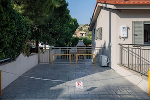 A gated entrance with a chain barrier, a paved pathway, and a building with a red roof and shutters.