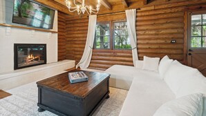 Ein Blockhaus-Interieur mit Kamin, einer großen weißen Couch und einem Holztisch.