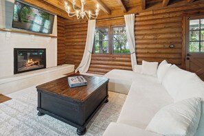 A log cabin interior with a fireplace, a large white sofa, and a wooden coffee table. - Waterfront Log home near Savannah Downtown (Liberty County)