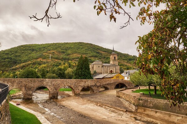 Un puente de piedra sobre un río, una colina con vegetación y un edificio con una torre.